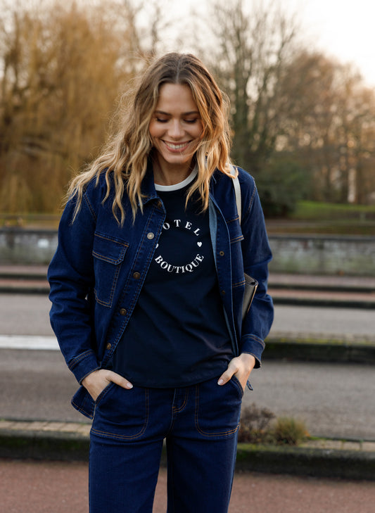 Donkerblauw t-shirt met ronde hals en wit bies, hotelboutique-opdruk zichtbaar bij de borst