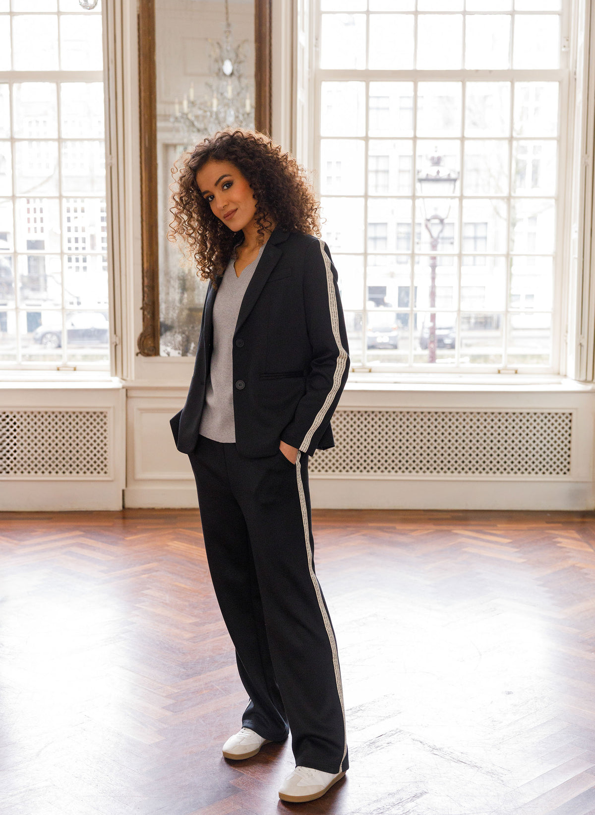 Zwarte blazer met revers en knoopsluiting, witte biezen langs mouwen.