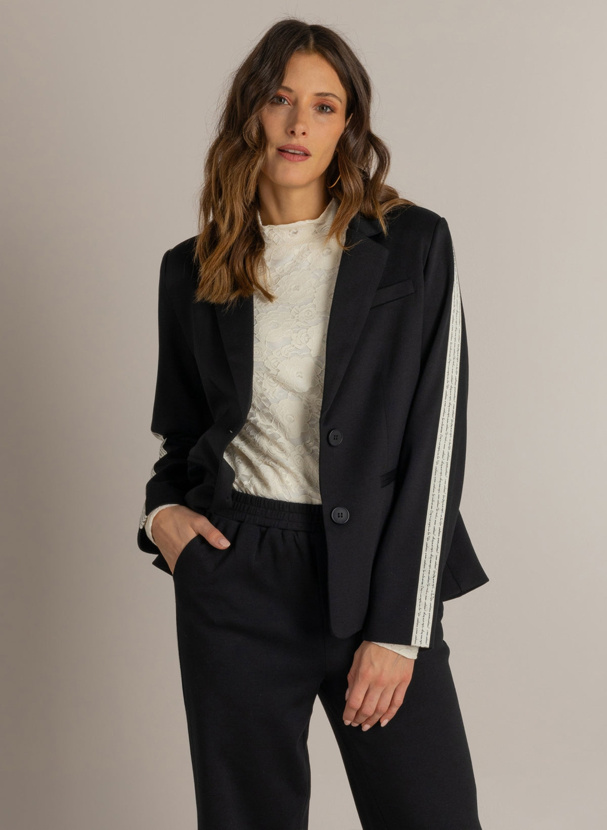 Zwarte blazer met revers en knoopsluiting, witte biezen op de mouw.