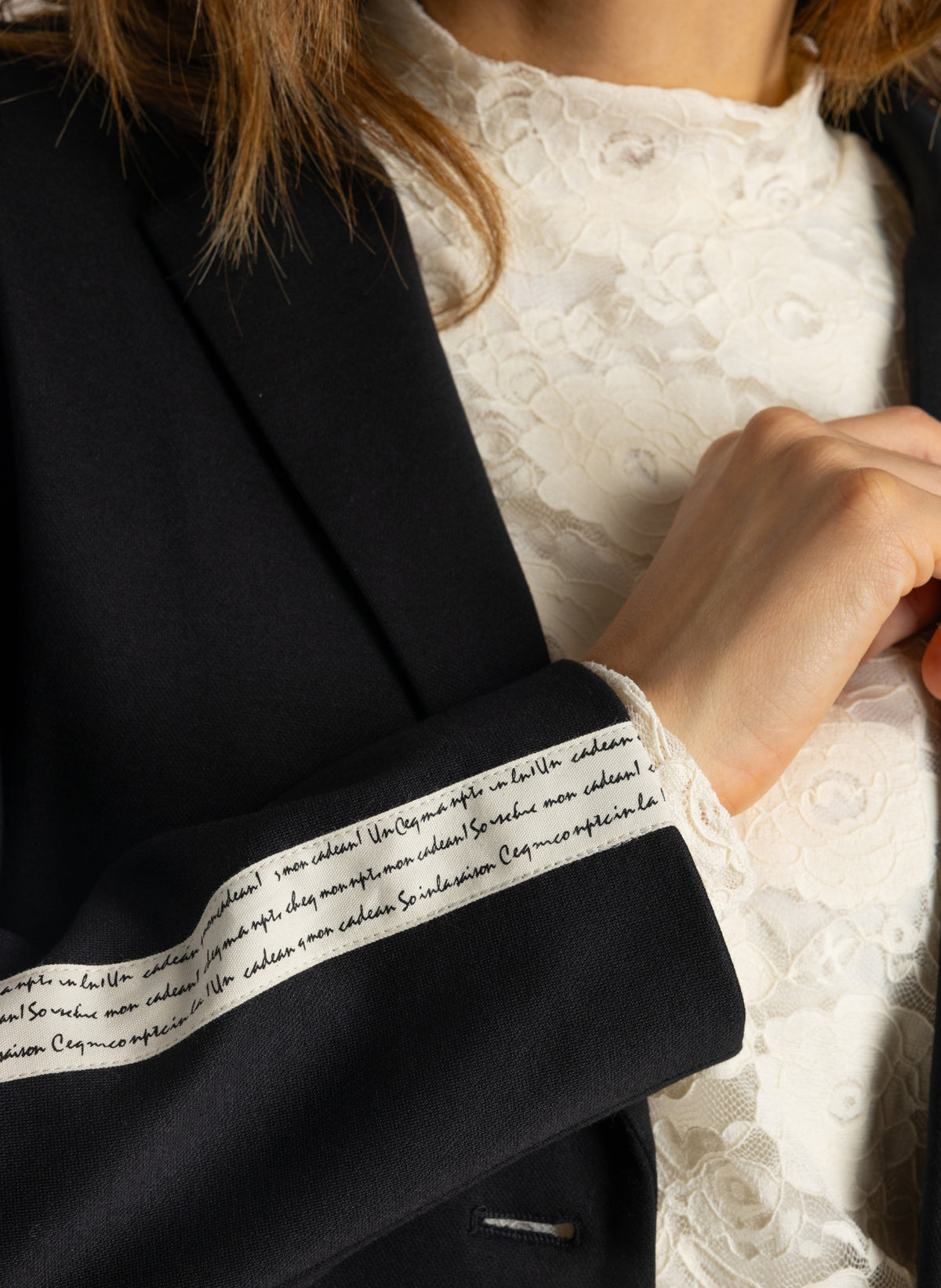 Detail zwarte blazer: witte bies en geborduurde tekst op binnenmanchet.