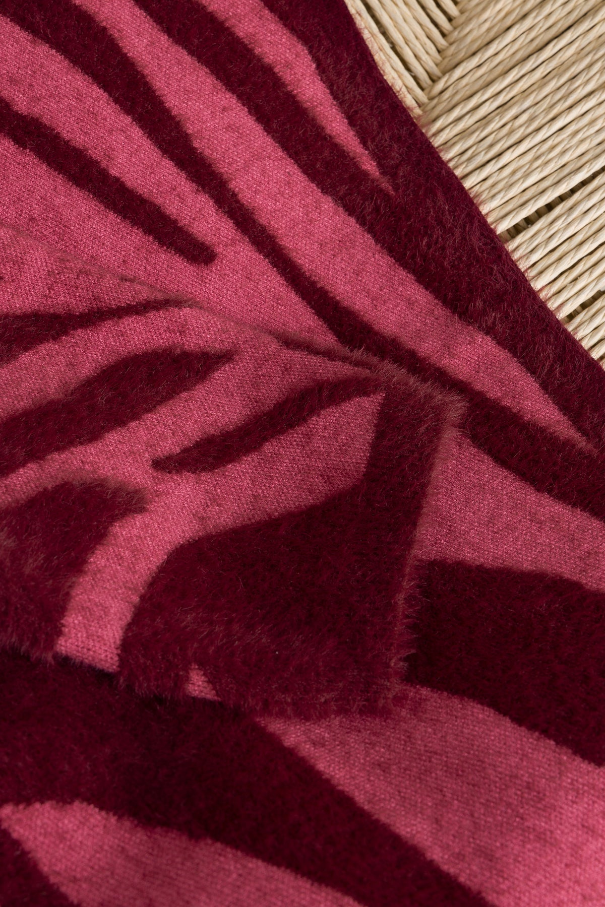 Close-up van donkerwijnrode stof met roze abstract gestreept patroon, zachte gebreide look.