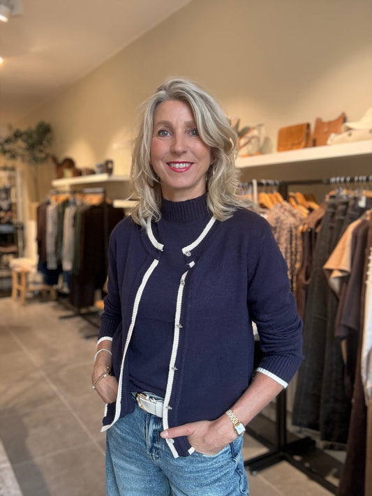 Donkerblauwe vest met rits en witte biezen, lange mouwen.