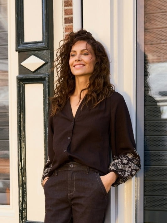 Donkere blouse met V-hals en knoopsluiting, lange mouwen met geborduurde boorden.